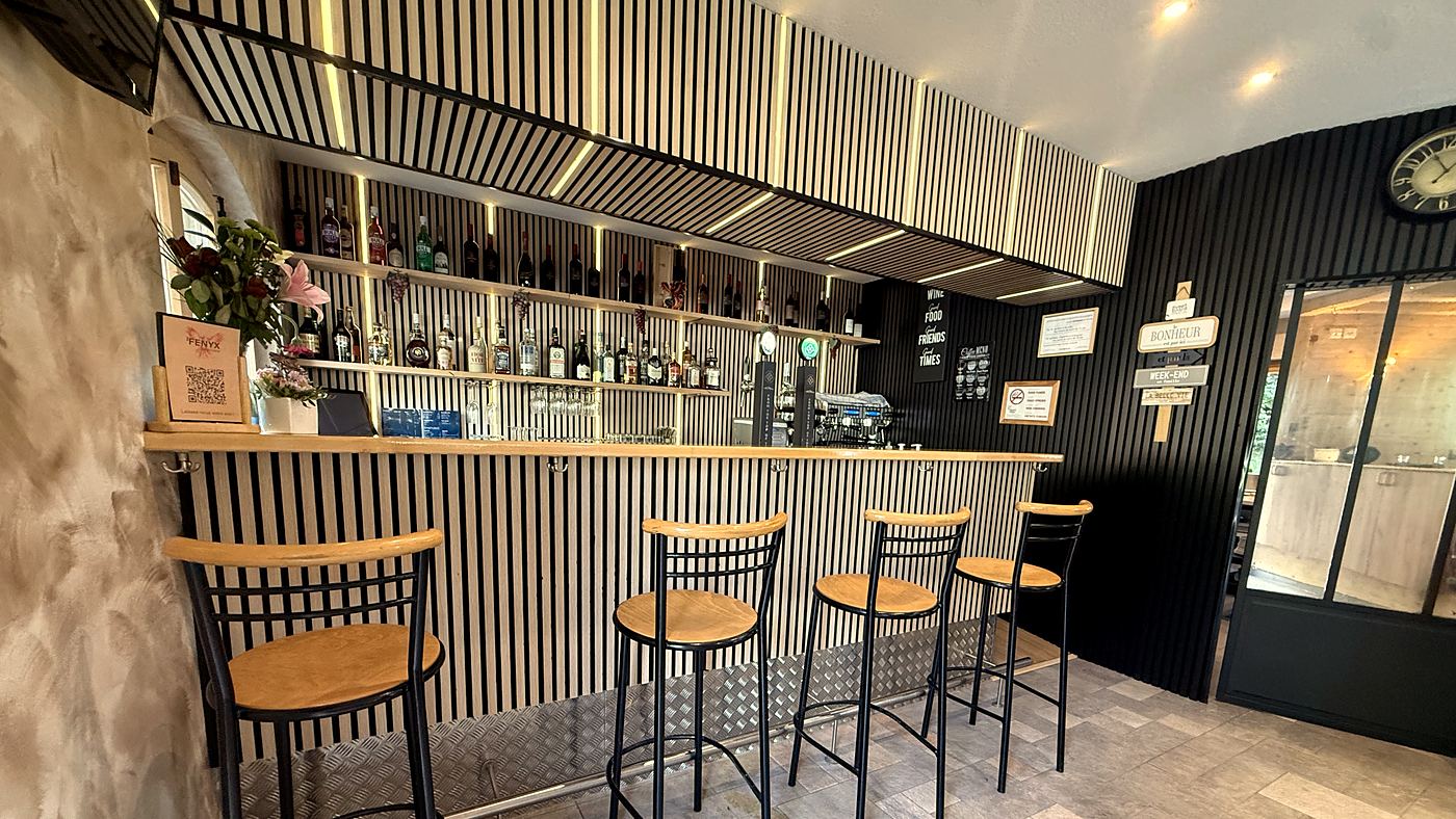Le bar en lattes de bois éclairées et ses tabourets