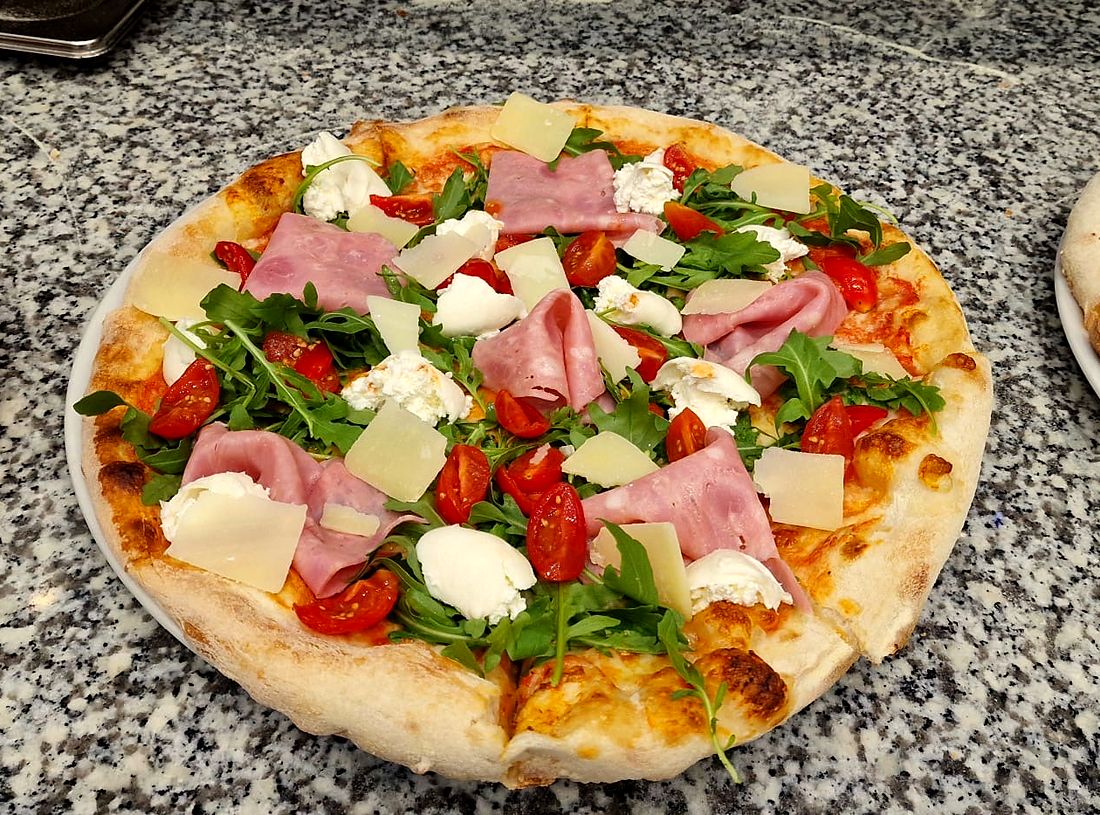 Pizza garnie de roquette, tomates cerises, mozzarella et copeaux de fromage